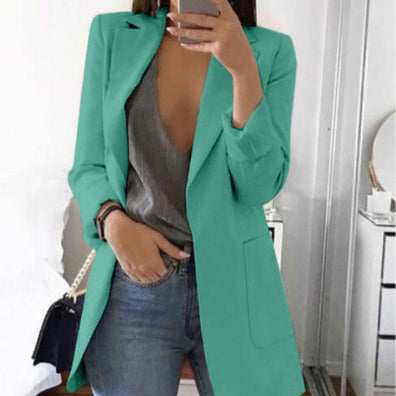 Woman wearing a teal open-front blazer with a grey top and jeans.