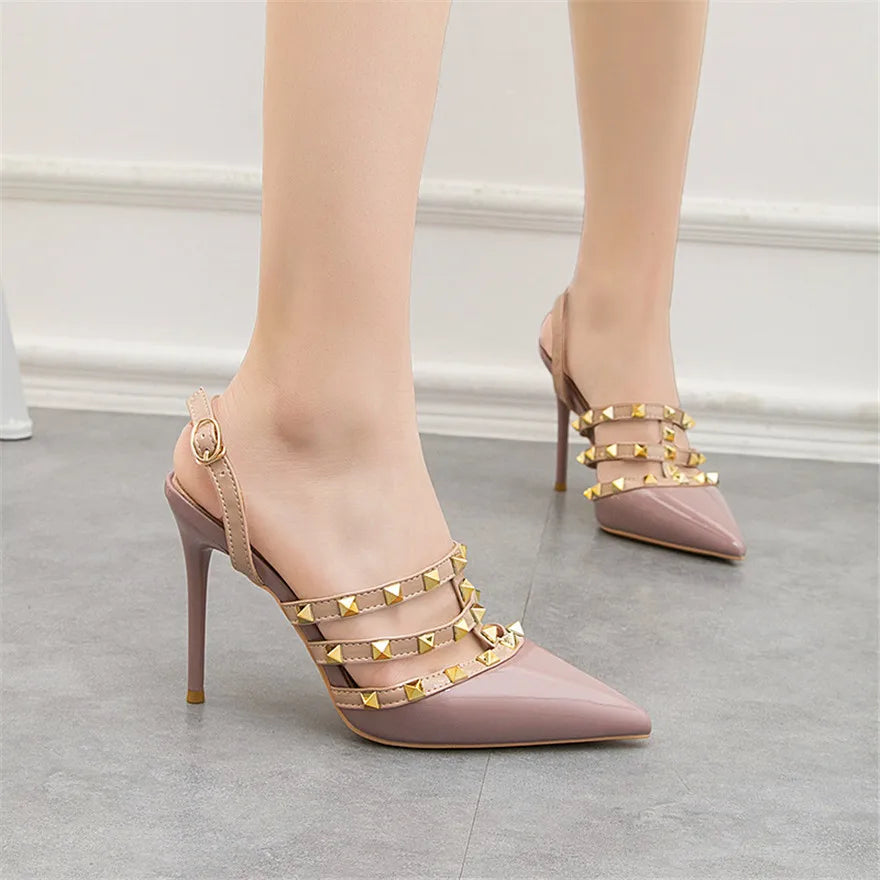 Nude patent pumps with gold rivet straps and ankle buckle. These strappy office shoes feature a pointed toe and heel.
