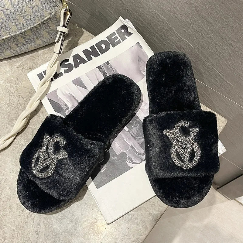 Black faux fur slippers with rhinestone logos and non-slip soles for cozy indoor house wear.