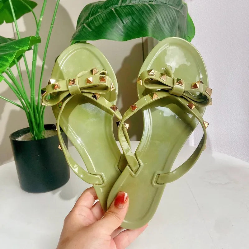Olive green jelly sandals with gold studded bows, a slip-on shoe design for comfortable everyday wear.