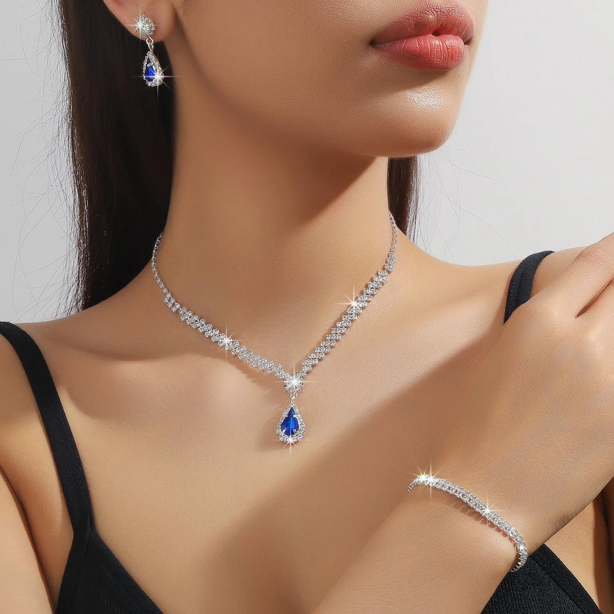Silver-tone necklace, earrings, and bracelet set with blue teardrop CZ crystal jewelry for weddings and events.