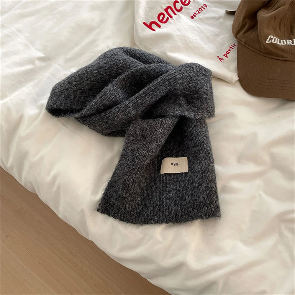 Dark grey knit scarf with a rectangular fabric patch, ideal for outdoor winter wear.
