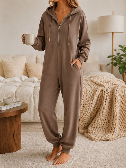 Model in a relaxed-fit hooded zip-up jumpsuit with ribbed cuffs, holding a mug