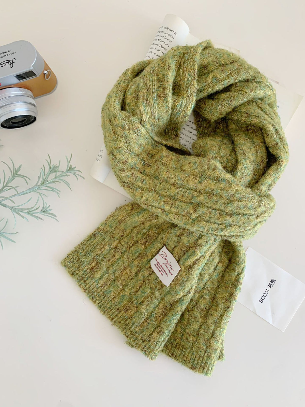 A chunky knitted green winter scarf with a textured cable weave lies flat on a surface.