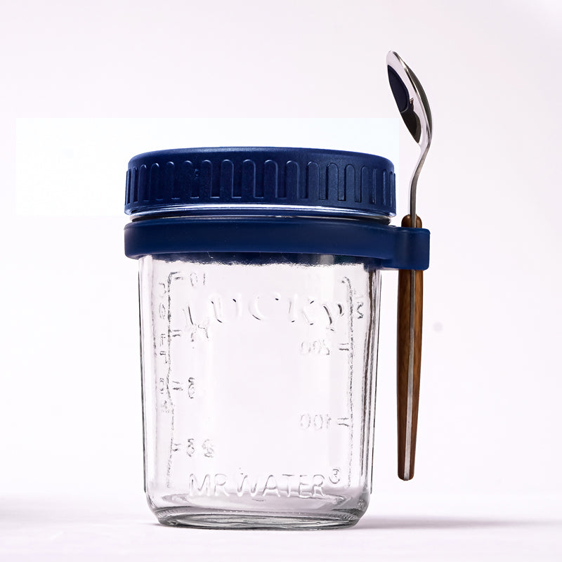 Glass overnight oats jar with blue lid, measurement markings, and a spoon held in a side silicone loop