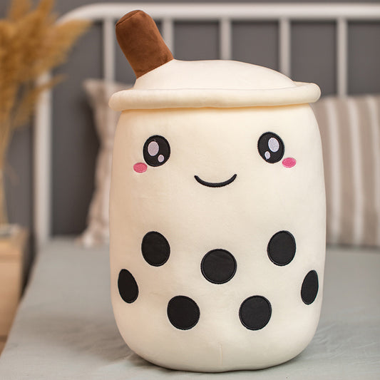 Stuffed food toy boba plush pillow with embroidered face and straw sitting on a bed