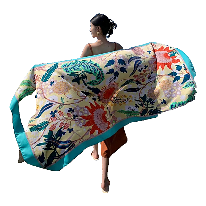 Women holding up a colorful printed beach sarong wrap scarf with blue border by the ocean