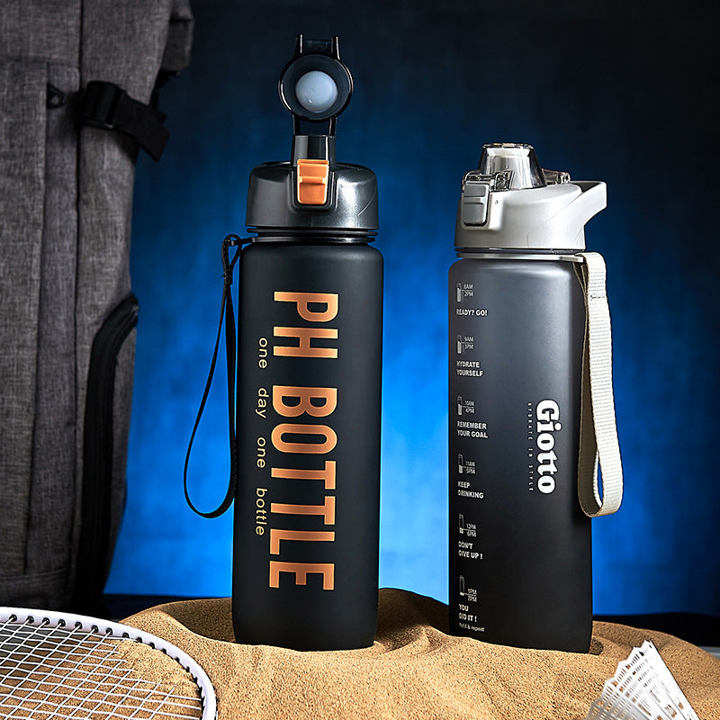Two sports water bottles with time markers stand on sand near a backpack and badminton racket.