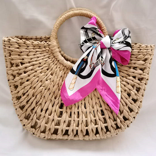 Beach tote bag woven from straw with round top handles and a decorative silk scarf tied on the handle