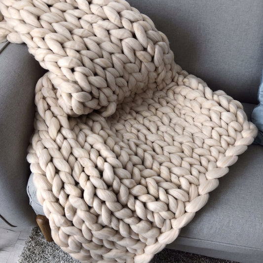 Cream chunky knit throw blanket draped over a grey living room sofa