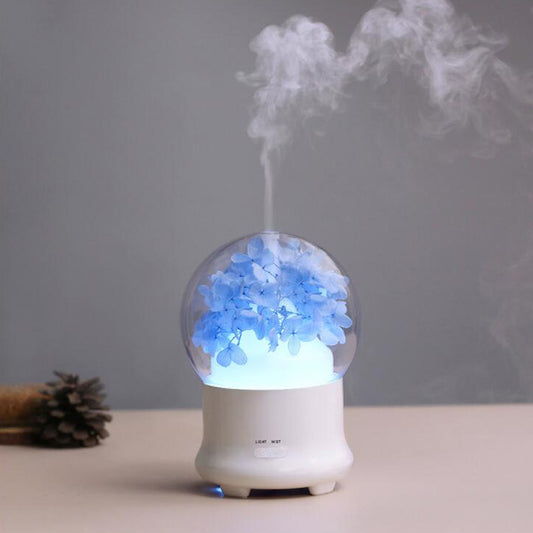 Round glass aroma diffuser with blue flowers inside releasing a cool mist.