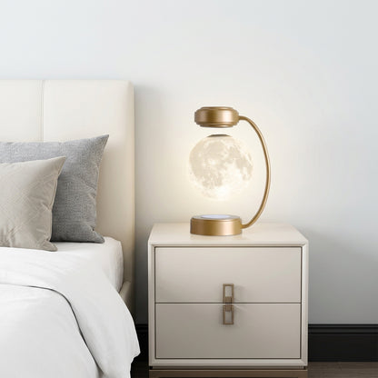 Gold levitating moon lamp on a nightstand beside a bed