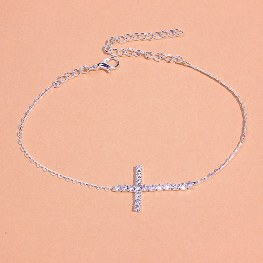 Silver chain anklet with a rhinestone-embedded cross pendant and lobster clasp.