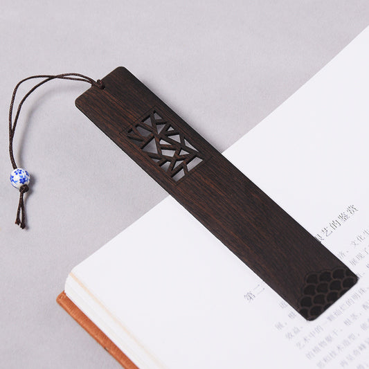 Dark wood bookmark with geometric cutout window resting on an open book, with a blue and white beaded cord.