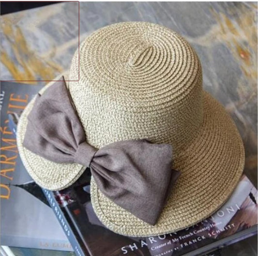 Tan straw bowler hat featuring a large brown fabric bow on the side, viewed from above.