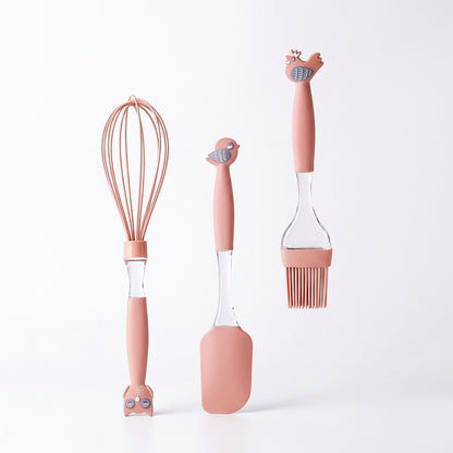 Three-piece pink silicone baking utensil set including a whisk, spatula, and basting brush with animal toppers.