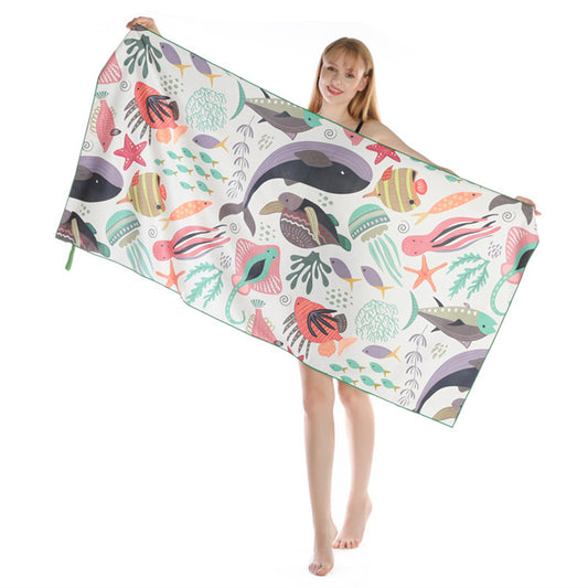 A woman holds up a beach towel with a colorful marine life and fish pattern against a white background.
