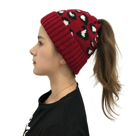 Profile of woman wearing red leopard-print knit beanie with ponytail opening and ribbed cuff.