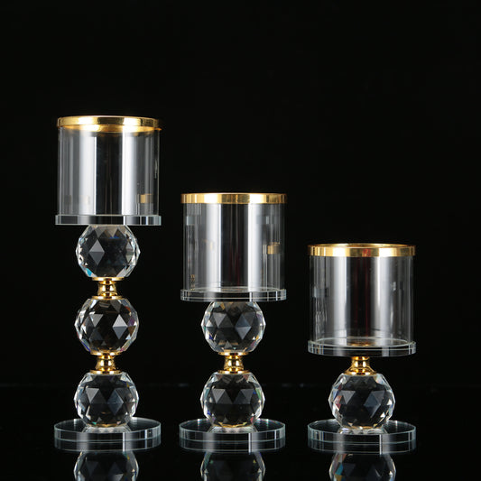 Three faceted crystal candle holders with gold rims and glass cylinder cups of varying heights.
