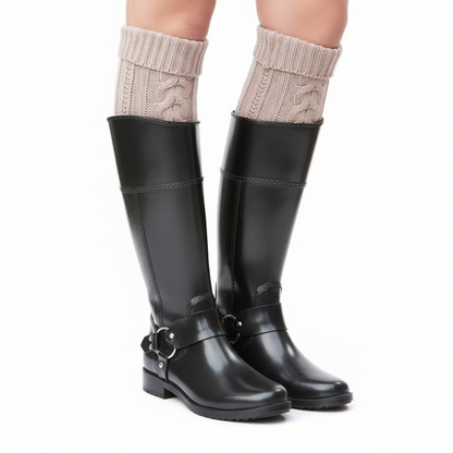 Black leather knee-high boots with side harness buckles and beige cable-knit boot cuffs on white.