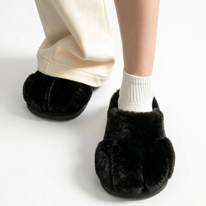 Person wearing black fluffy slippers with toe indentations, white ankle socks, and beige trousers.