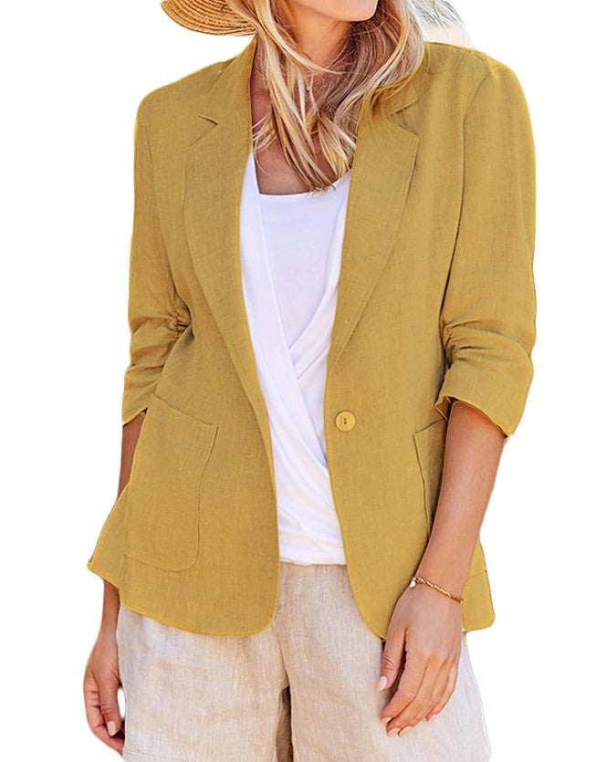 Woman wearing an open mustard yellow single-button blazer over a white top and light pants.