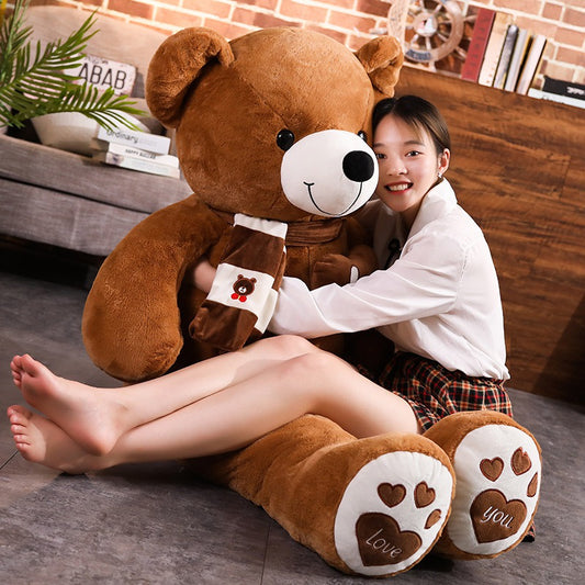 Stuffed animal teddy bear plush toy with scarf and heart paw prints hugging a smiling person