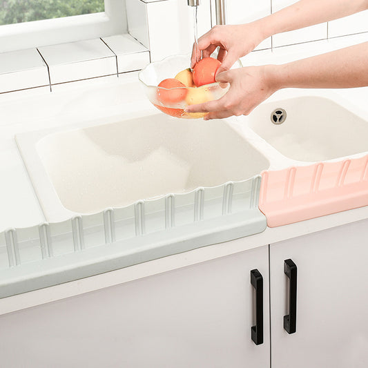 Sink splash guards in green and pink attached to kitchen counter while washing fruit