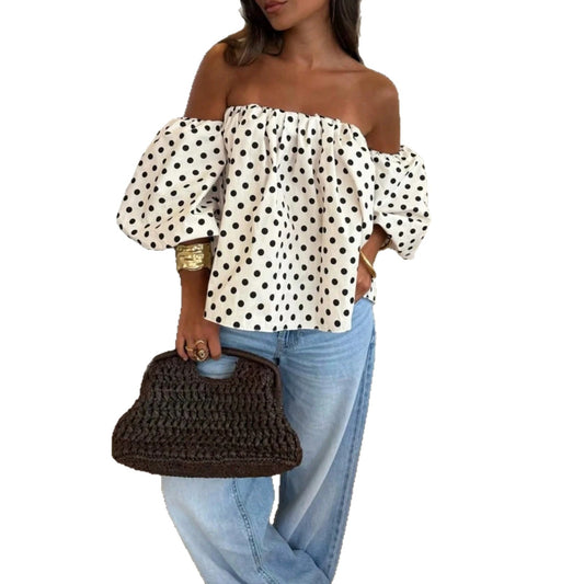 Woman wearing an off-shoulder polka-dot blouse with lantern sleeves and light-wash jeans, holding a woven dark brown bag.