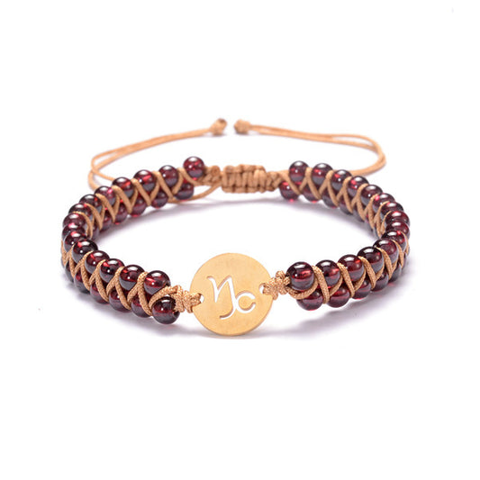 Woven cord bracelet with dark red beads and a gold-tone zodiac disc charm.