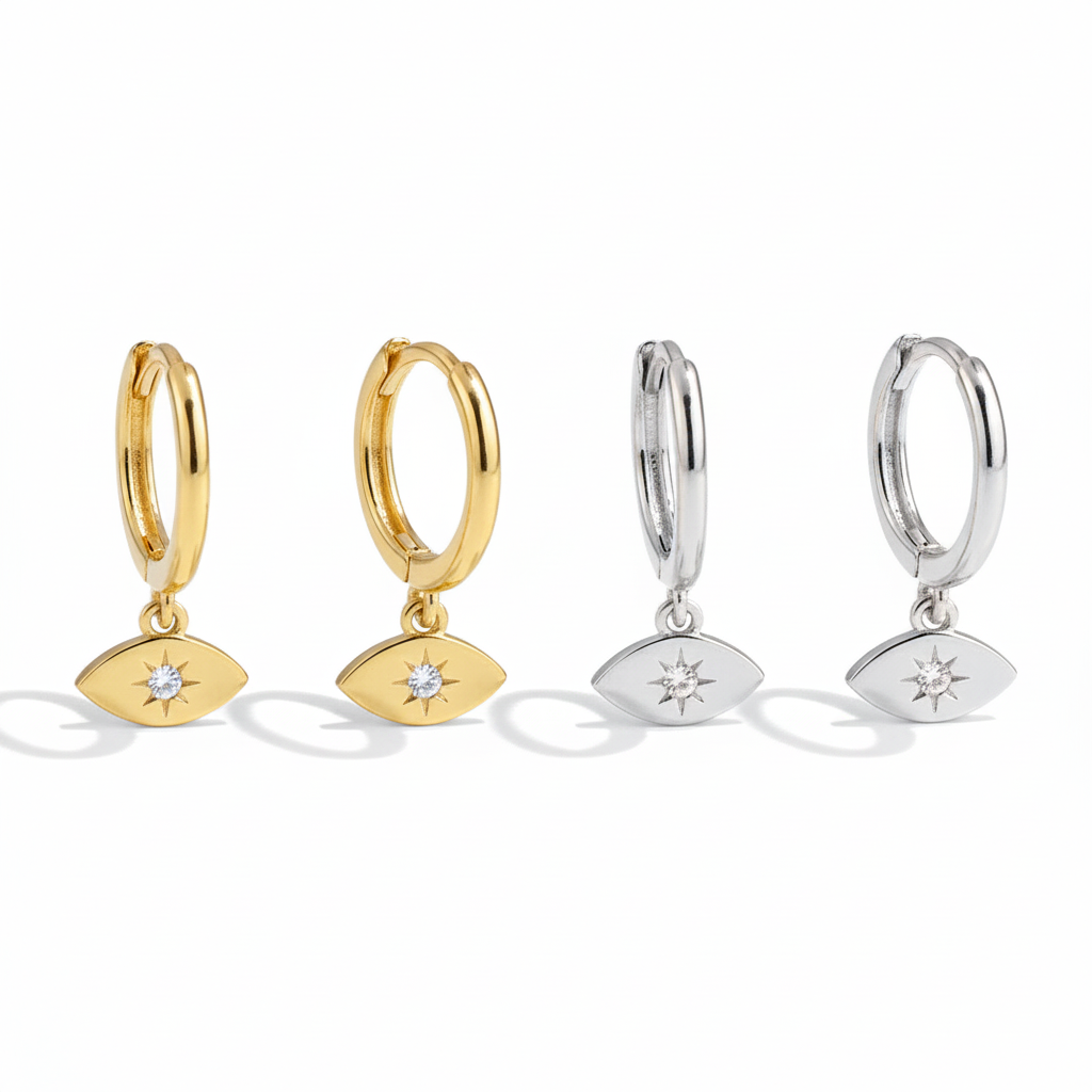 Four metal hoop earrings featuring evil eye charms with center crystal starbursts, shown in gold and silver against white.