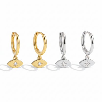 Four metal hoop earrings featuring evil eye charms with center crystal starbursts, shown in gold and silver against white.