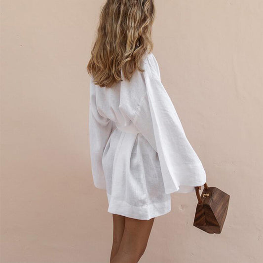 Back view of a woman wearing a white linen wrap top with wide sleeves and holding a wooden handbag.