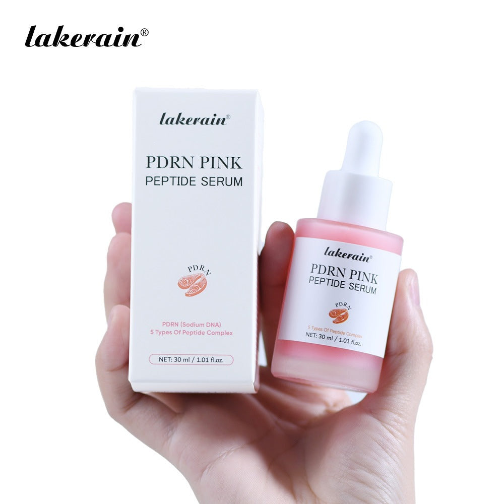 A hand holding a white box and a glass bottle of pink PDRN peptide face serum with a dropper.