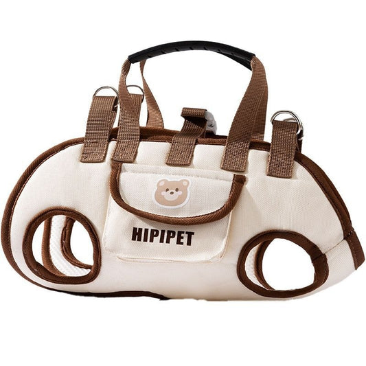 Beige and brown pet carrier sling with dual leg holes, top handle, and a small front pocket featuring a bear patch.