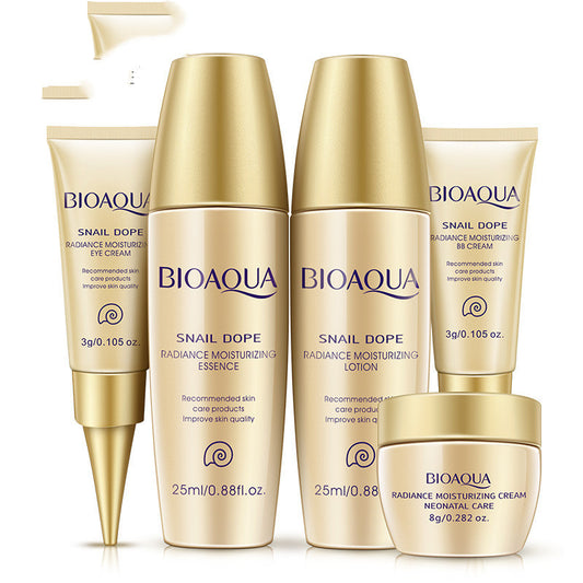 Skincare set with two bottles, two tubes, and a cream jar in gold and cream packaging against a white background.