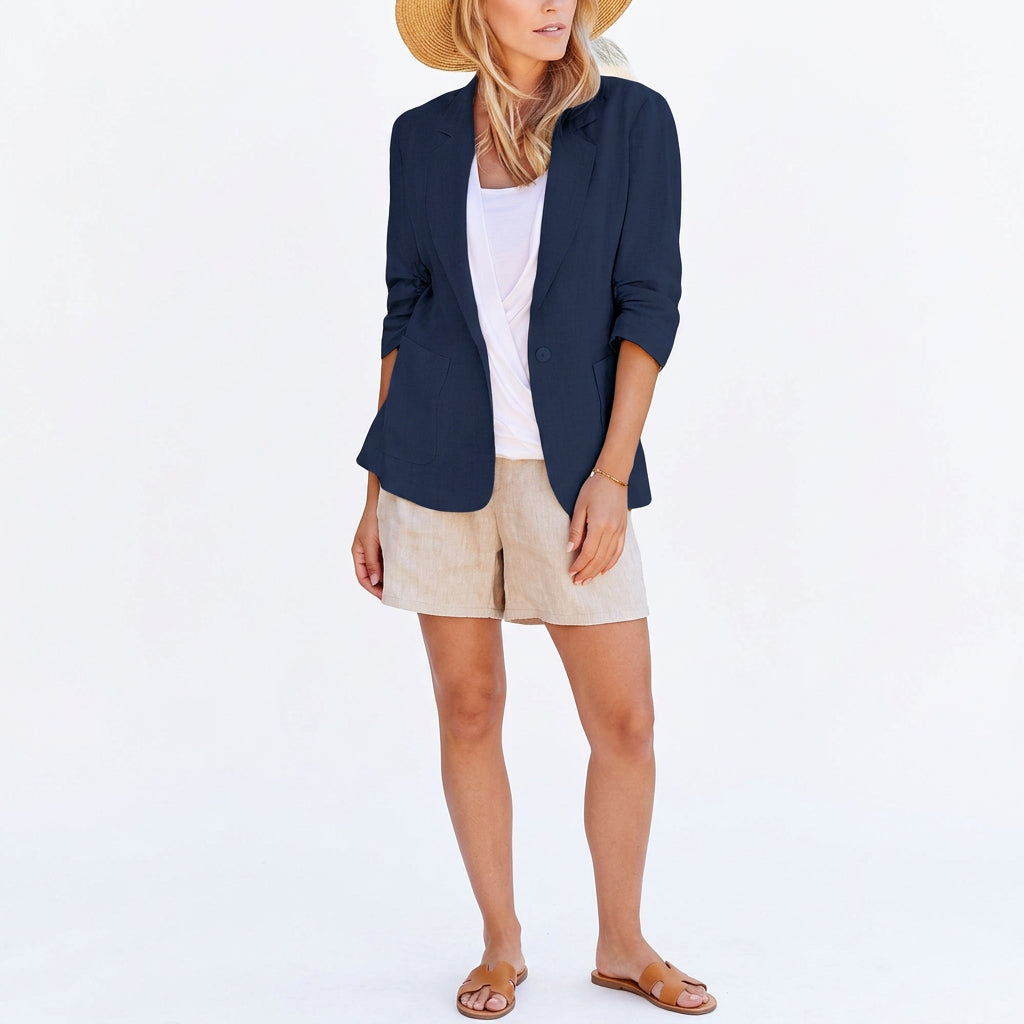 Woman wearing a navy blue single-breasted suit jacket over a white top and tan shorts.