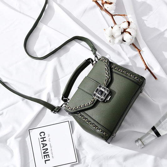 Dark green structured shoulder bag with chain trim and top handle on white fabric.