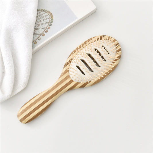 Striped wooden vent hair brush with plastic bristles next to a white towel and book.