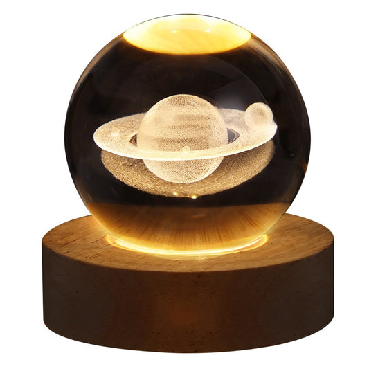 Engraved crystal ball night light featuring Saturn with rings, resting on an illuminated round wooden base.