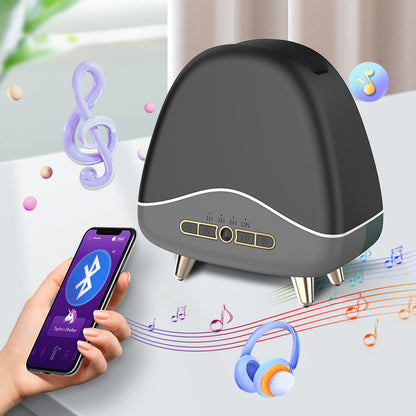 Black aroma diffuser on four legs next to a hand holding a smartphone showing a Bluetooth app.