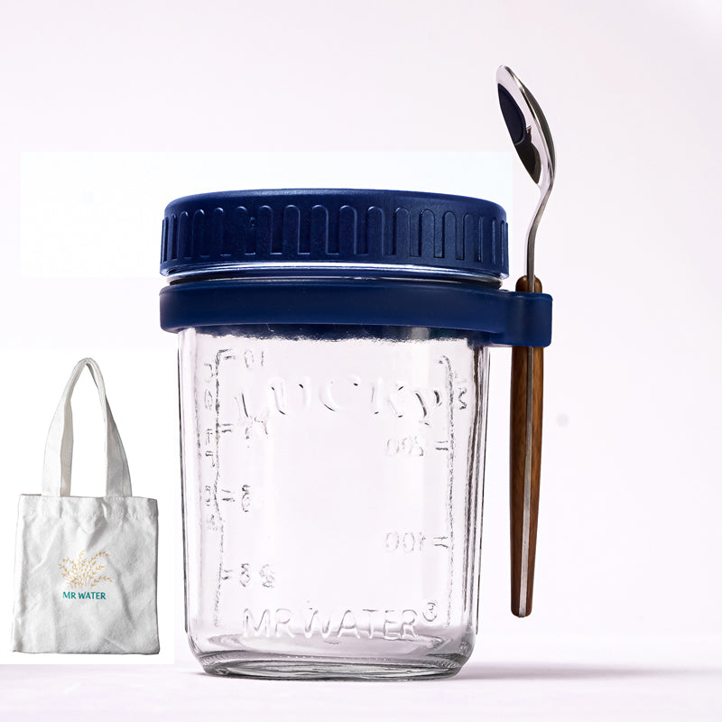 Glass jar with blue lid, measuring markings, spoon in side holder, and a small tote bag.