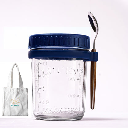 Glass jar with blue lid, measuring markings, spoon in side holder, and a small tote bag.