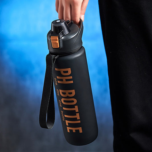 Person holding a matte black water bottle with a black carrying strap, orange lid latch, and large orange text.