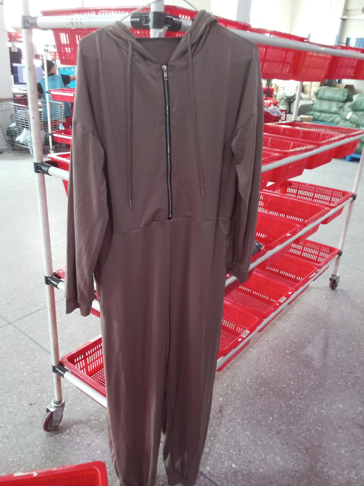 Hooded zip-up jumpsuit hanging on a clothing rack among storage baskets