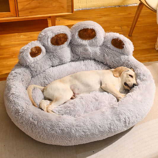 Fluffy grey paw-shaped dog bed with high bolsters and a light-colored dog sleeping inside on wooden flooring