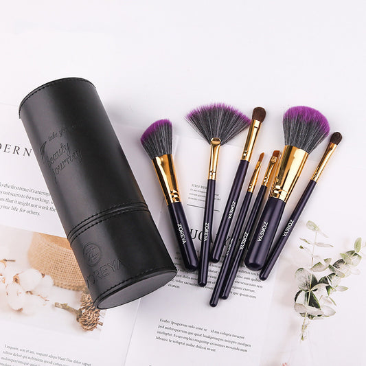 Makeup brush set with purple-tipped bristles, gold ferrules, and a black cylinder holder.