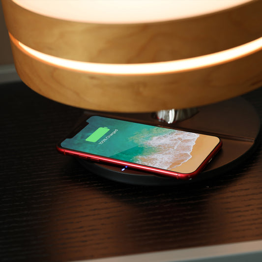 Smartphone charging wirelessly on the base of a wooden bedside lamp.
