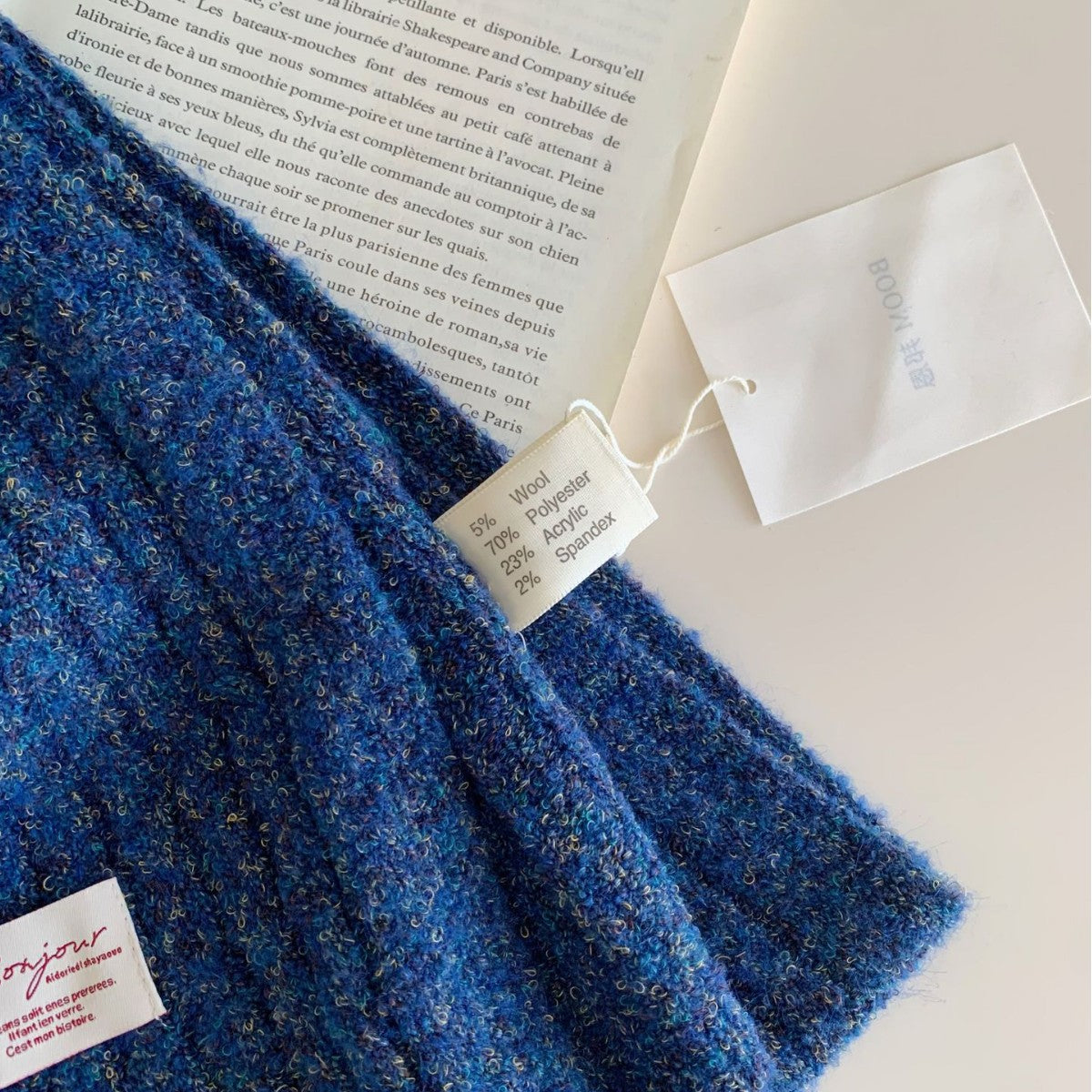 Close-up of blue textured knitted scarf showing material tag with wool and polyester blend.