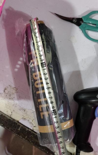 Water bottle in plastic wrapping measured with a tape measure on a table.